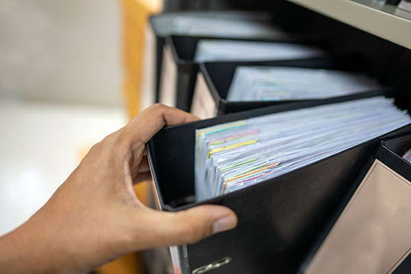 A hand grabs black binder full of documents off shelf.