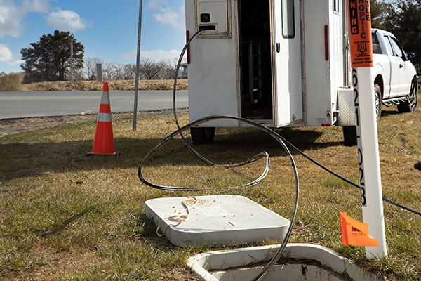 White truck extends a fiberoptic cable into the ground.