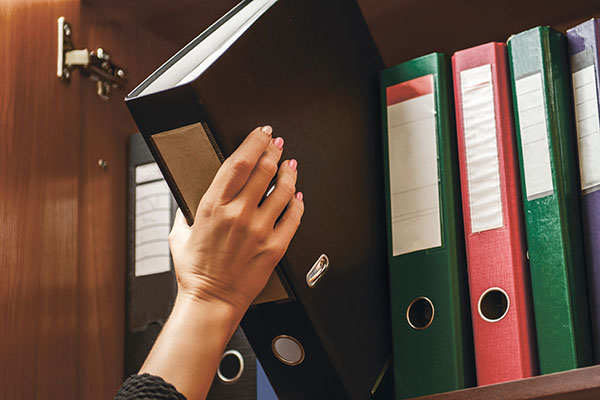 hand picks a binder of documents from a shelf with other binders.